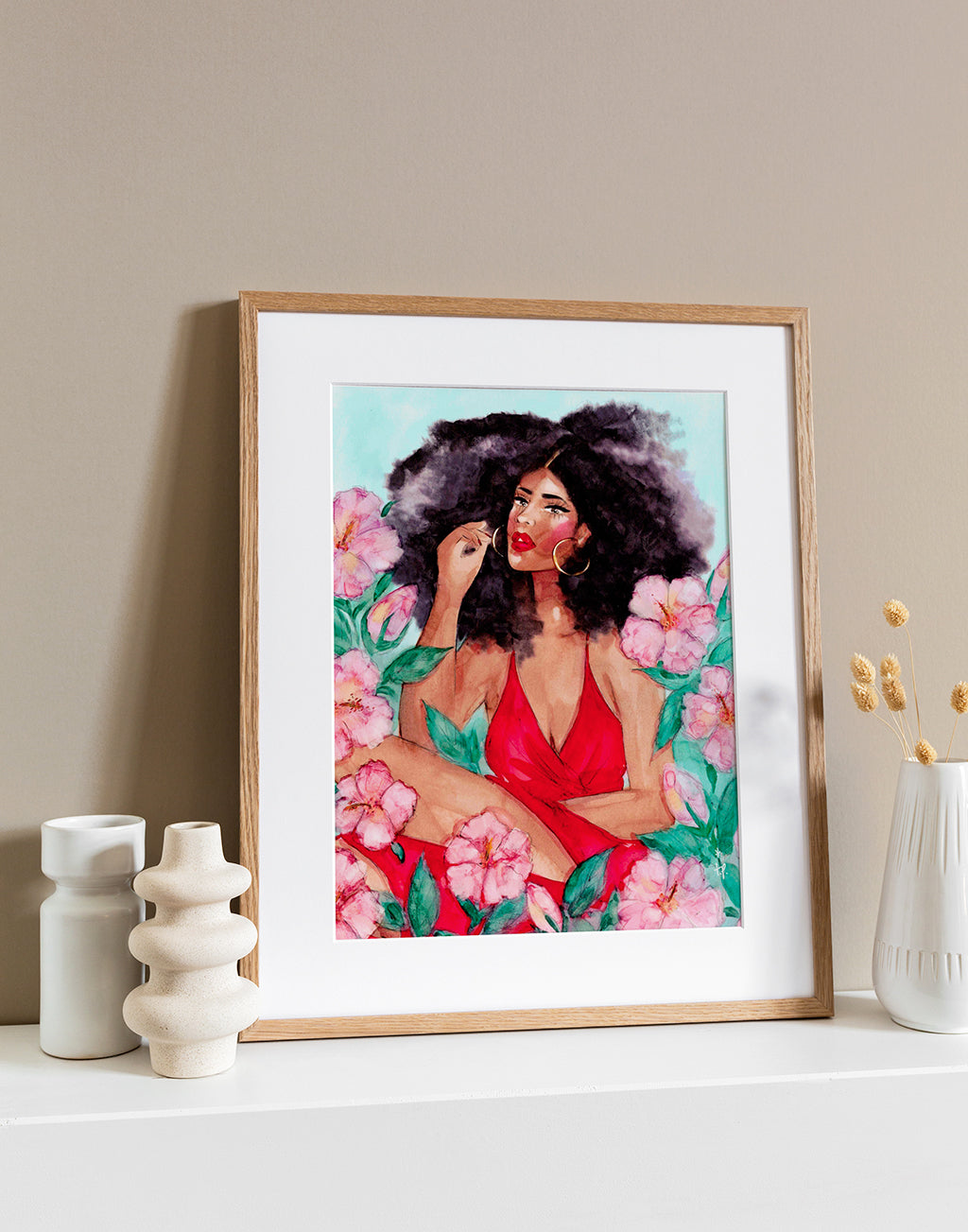 Illustration in a light frame of a beautiful black woman wearing a red dress and sitting among hibiscus flowers by Tatiana Poblah